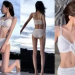 Sheon from the K-pop group Billlie posing for a photo in a white swimsuit on a sunny Jeju beach, with a clear blue sea background.