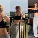 Jeon Somi posing on a terrace overlooking the ocean in a bra top and gray sweatpants