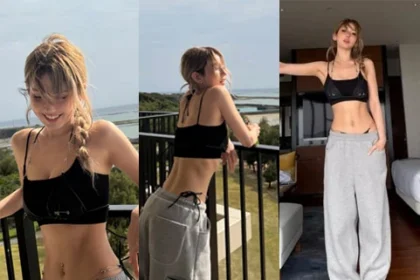 Jeon Somi posing on a terrace overlooking the ocean in a bra top and gray sweatpants