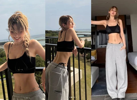 Jeon Somi posing on a terrace overlooking the ocean in a bra top and gray sweatpants